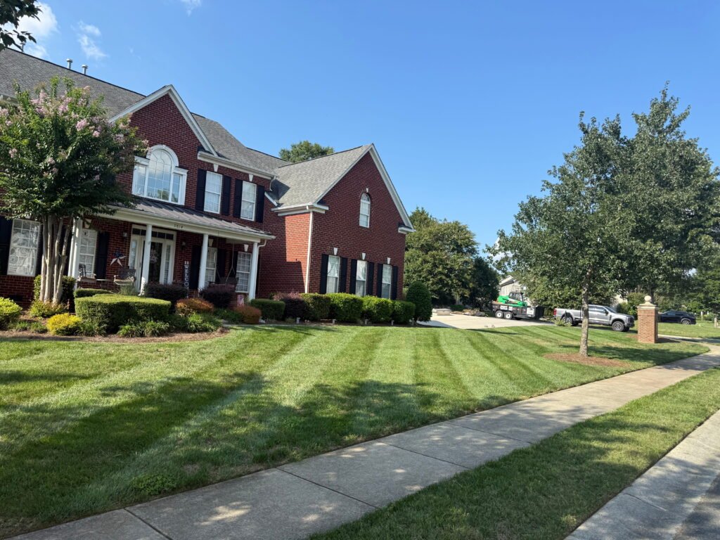 Professional lawn mowing service featuring clean-cut stripes on a lush green front yard of a brick home.